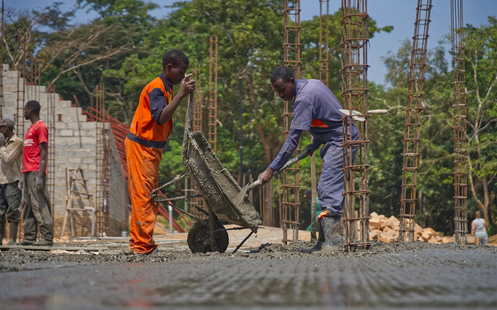 Crew pouring concrete with wheelbarrow and hand tools